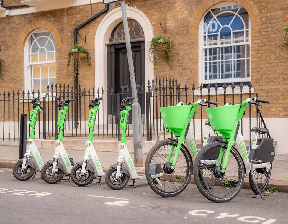 Lime scooters and bikes parked together beside a pavement